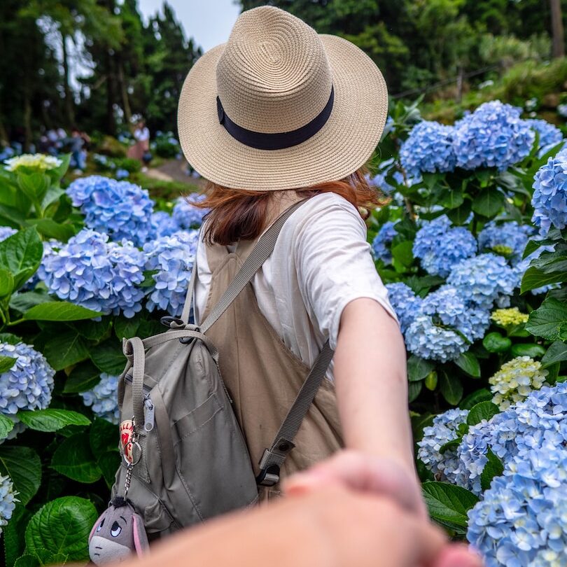 woman in white shirt and brown hat standing near blue flowers during daytime